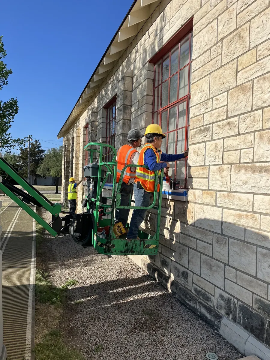 RCC crew on boom lift restoring red window trim on historic limestone building