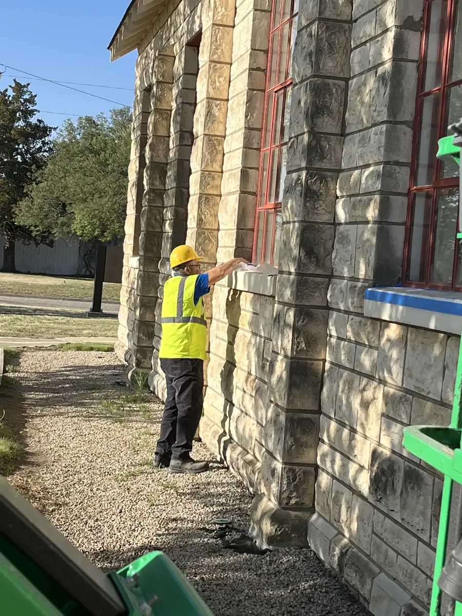 RCC crew member inspecting and detailing window frame on stone building facade