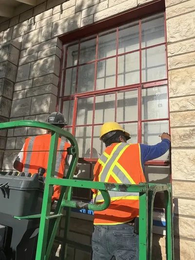 Two RCC technicians on lift restoring window frames on limestone facade